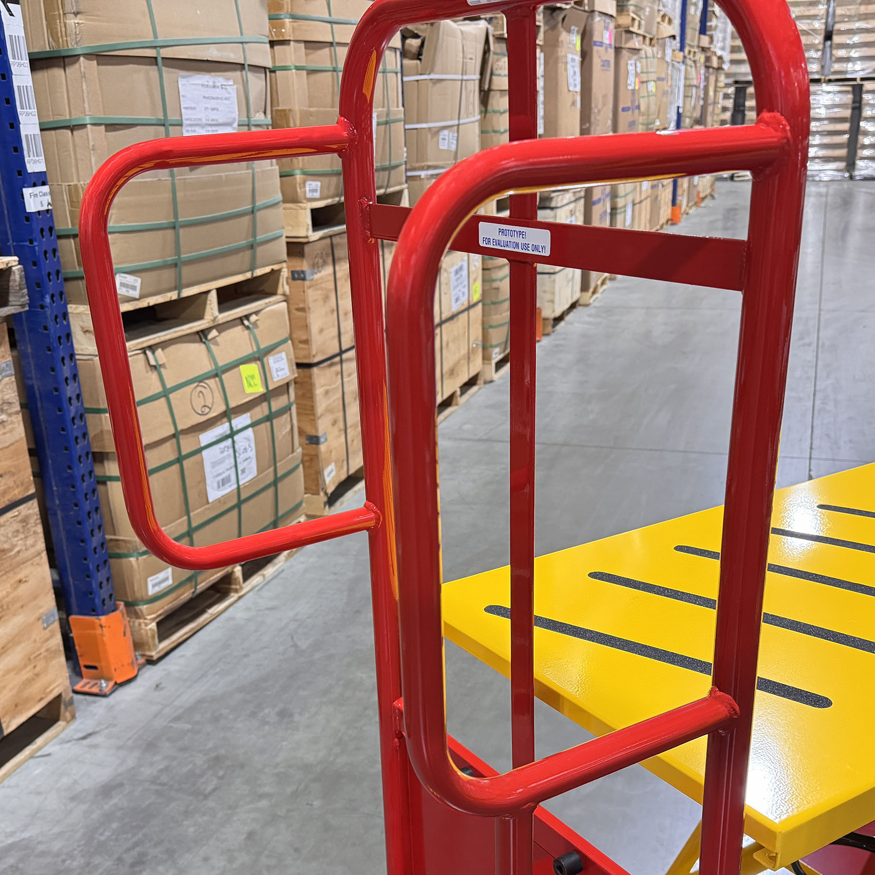 Spring-loaded lift table order picking cart designed to maintain an ergonomic working height. Ergonomic warehouse order picker with integrated safety step for elevated access. Heavy-duty spring lift platform cart built for industrial order fulfillment. Non-slip platform improves safety during warehouse picking and restocking. Order picking cart with guardrails and safety step for secure material handling.
