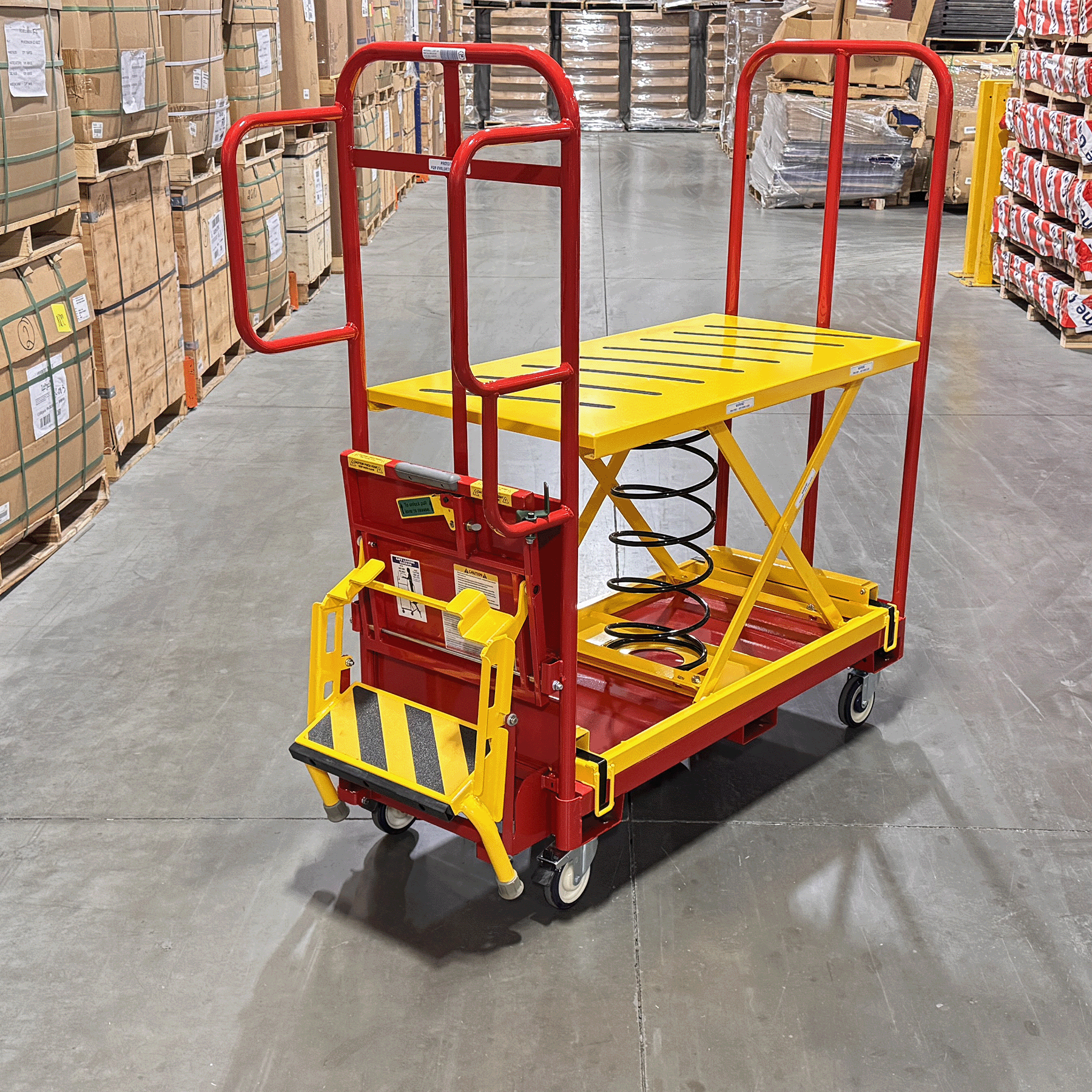 Spring-loaded lift table order picking cart designed to maintain an ergonomic working height. Ergonomic warehouse order picker with integrated safety step for elevated access. Heavy-duty spring lift platform cart built for industrial order fulfillment. Non-slip platform improves safety during warehouse picking and restocking. Order picking cart with guardrails and safety step for secure material handling.